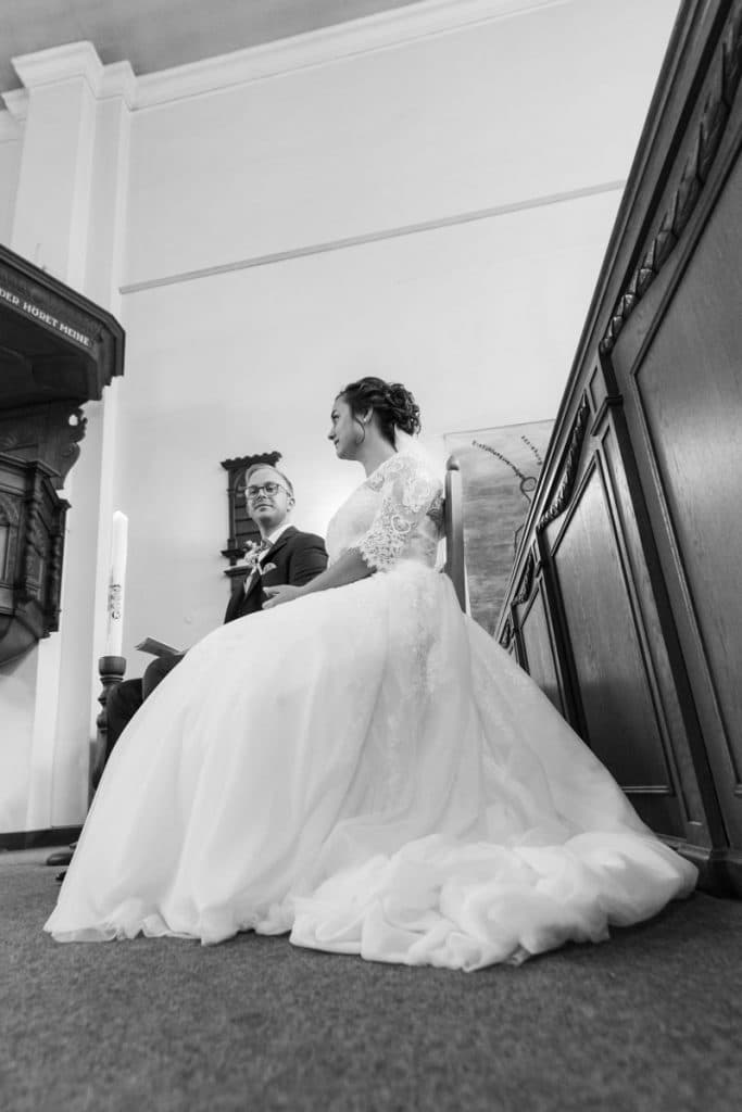 Emotionaler Moment bei der kirchlichen Trauung in der Evangelischen Kirche am Markt in Xanten: Das Brautpaar steht gemeinsam am Altar, die Braut im weißen Spitzenkleid mit Schleier, der Bräutigam im eleganten Anzug. Gäste verfolgen die Zeremonie aufmerksam in der festlich geschmückten Kirche. Dieses Foto zeigt die authentische Hochzeitsreportage vom Hochzeitsfotograf Xanten.