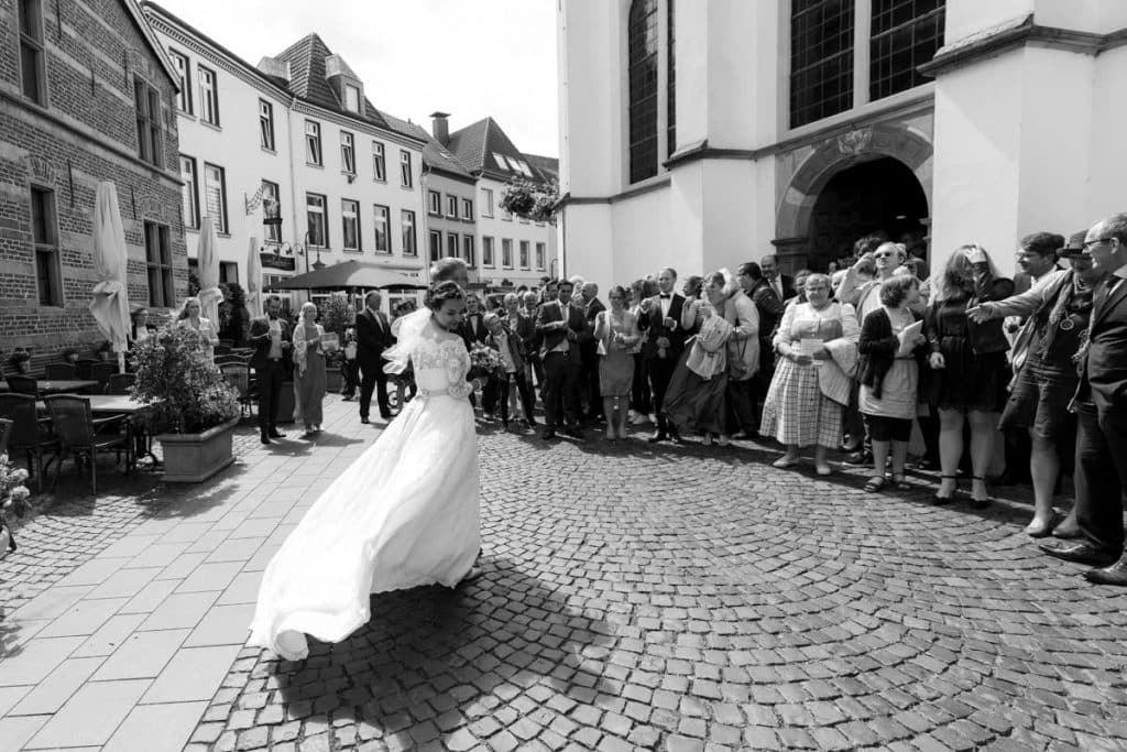 Emotionaler Moment bei der kirchlichen Trauung in der Evangelischen Kirche am Markt in Xanten: Das Brautpaar steht gemeinsam am Altar, die Braut im weißen Spitzenkleid mit Schleier, der Bräutigam im eleganten Anzug. Gäste verfolgen die Zeremonie aufmerksam in der festlich geschmückten Kirche. Dieses Foto zeigt die authentische Hochzeitsreportage vom Hochzeitsfotograf Xanten.
