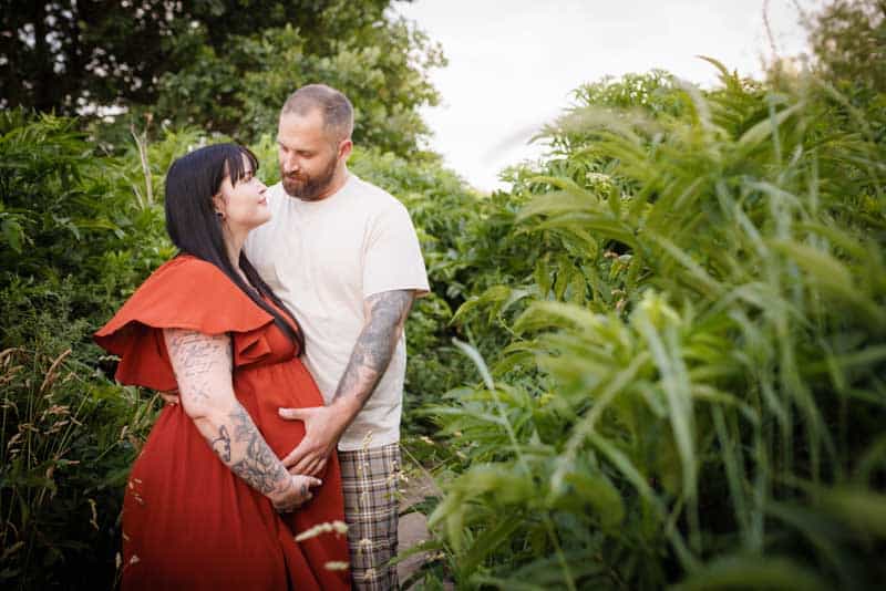 Babybauchshooting in der Natur: Schwangere Frau im roten Kleid mit Partner im Grünen, fotografiert von Fotograf Martin Valk in Dinslaken und am Niederrhein